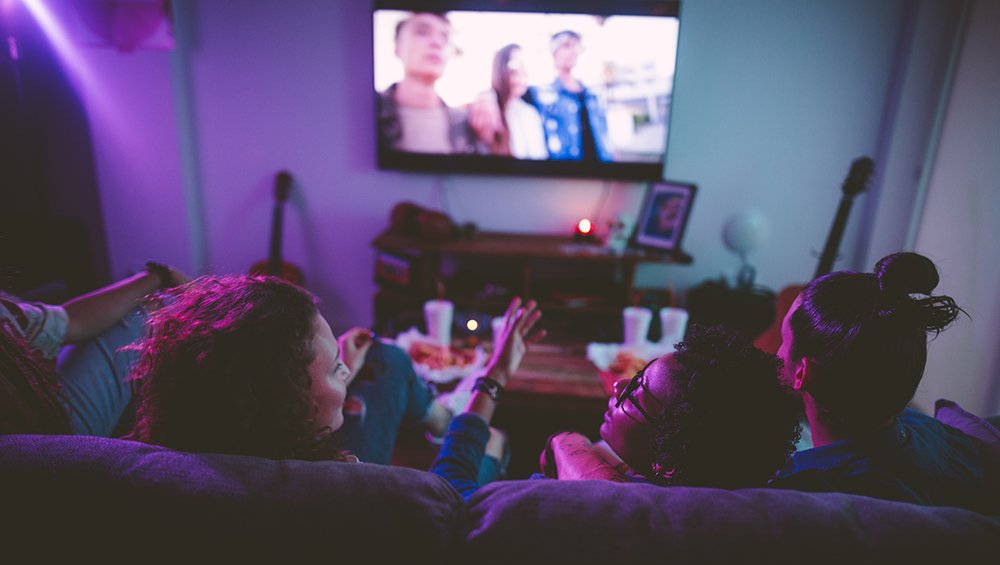 Multi-ethnic teenage friends watching TV together at hangout house