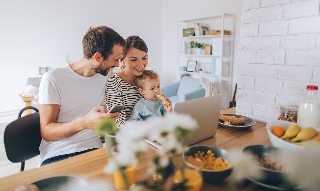 couple and young son having breakfast on smartphone and laptop