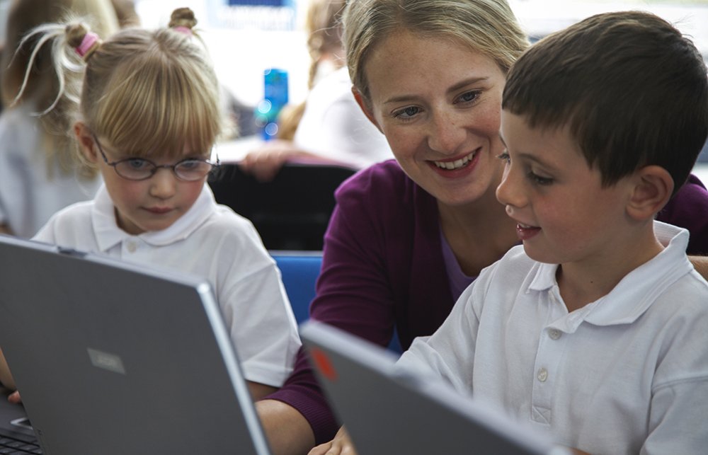 Female teacher helping boy (3-5) in computer class, smiling