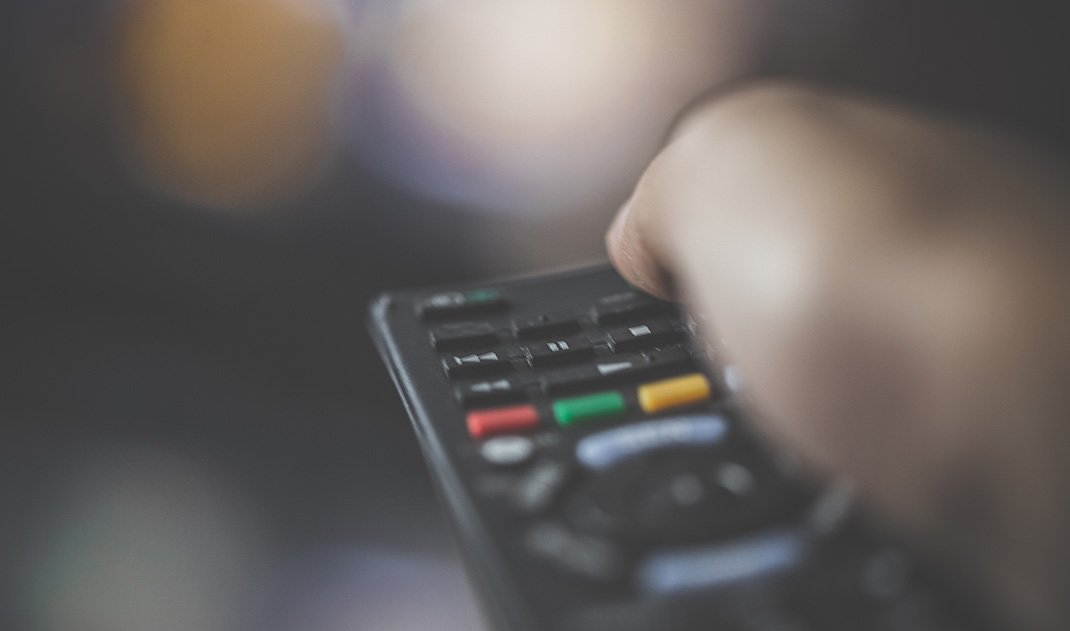 Person handling the remote control of a Television unit to change the channel or control the volume