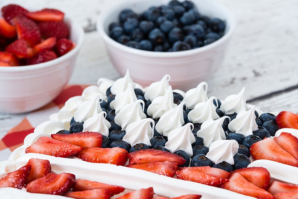 Patriotic American flag cake. Bowls of blueberries and strawberries in the background.