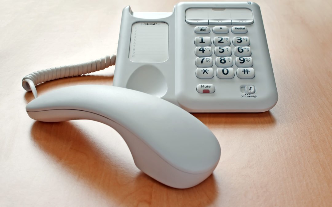Telephone on an window lit office desk with the receiver off the hook and the call on hold