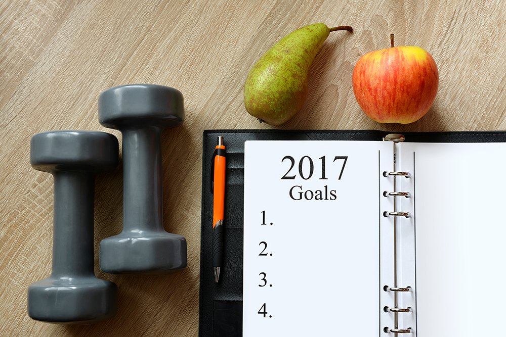 Dumbbells with fruits and open notebook on wooden desk. Healthy resolutions for the New Year 2017.